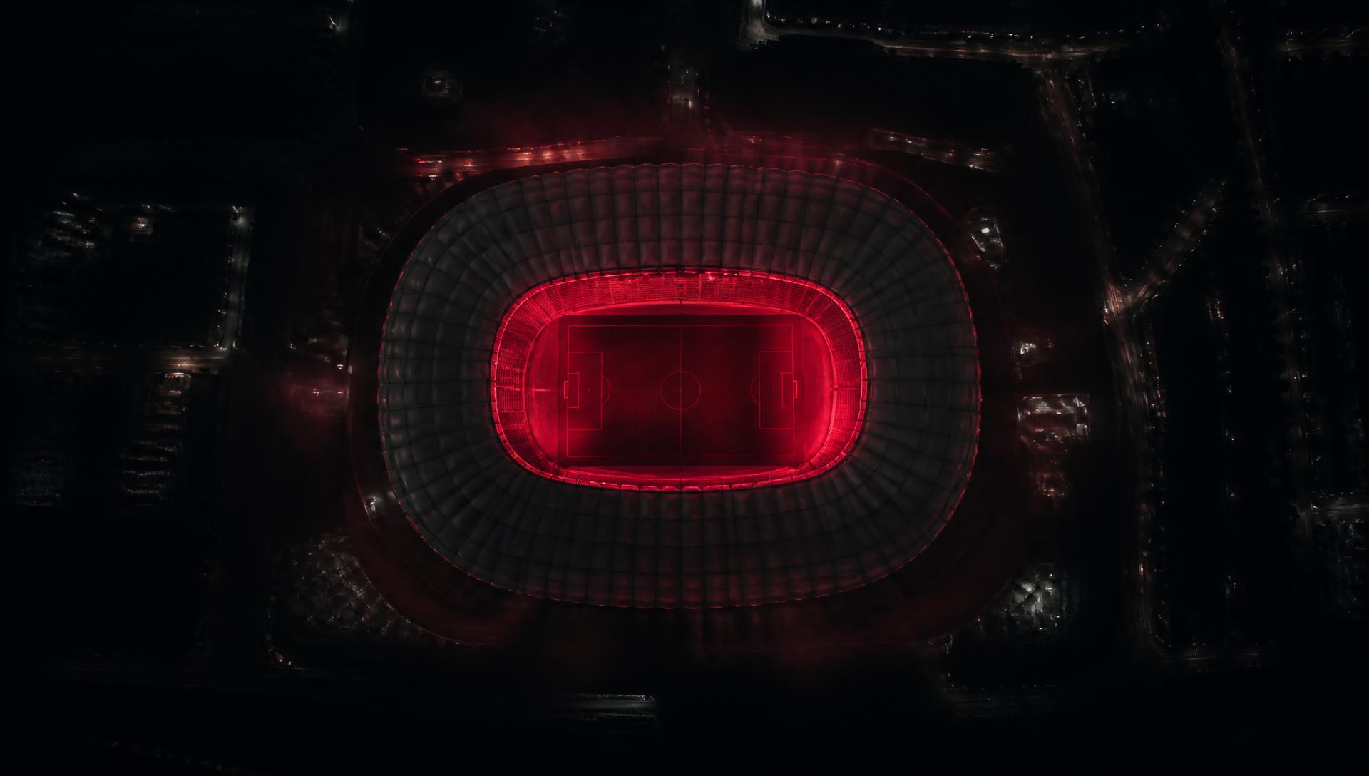 Vista aérea noturna do estádio iluminado em vermelho